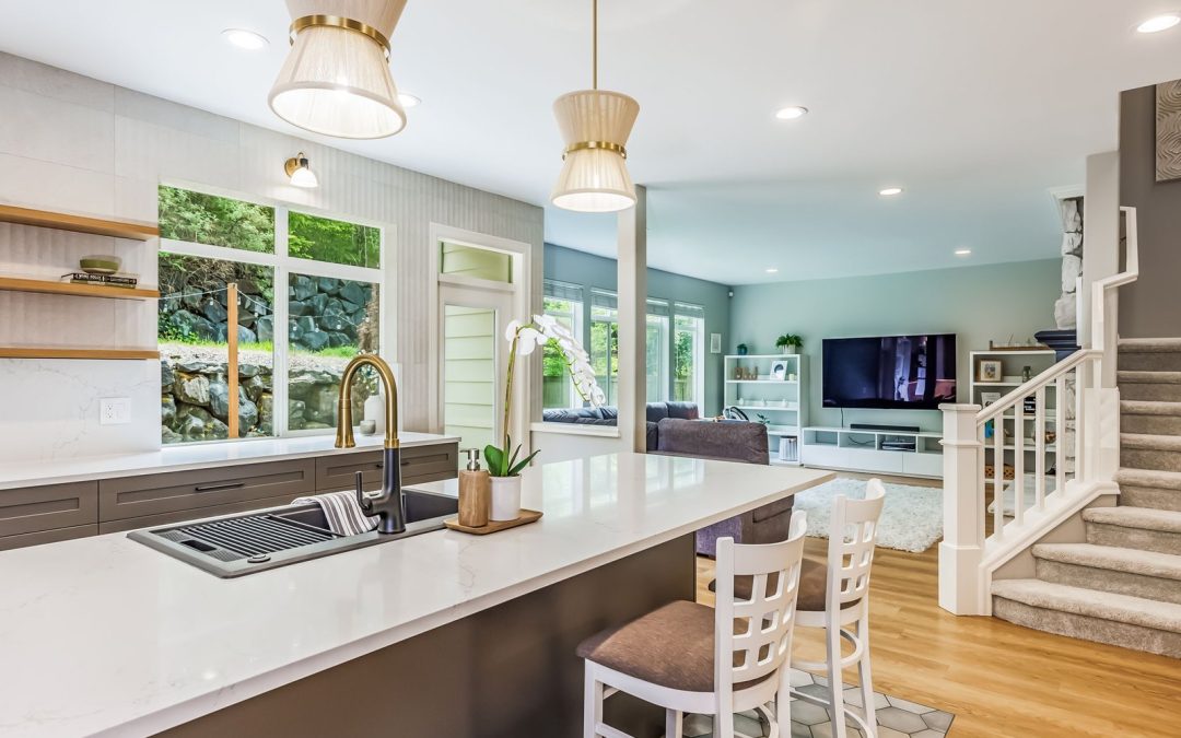 Open concept kitchen island with brass and black faucet, pleated pendants and living room beyond